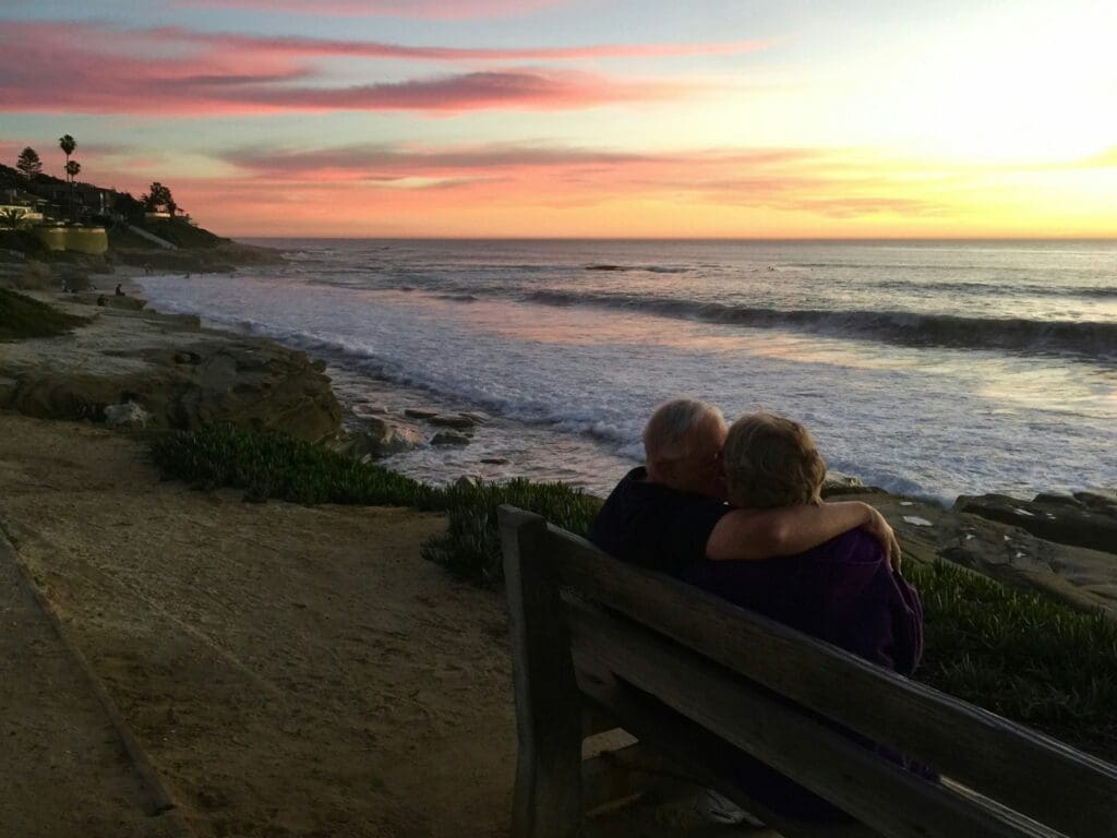 man and woman sitting on brown wooden bench in front of shoreline