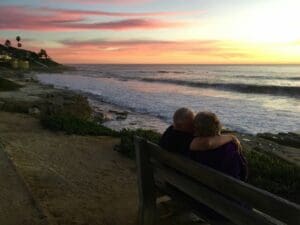 man and woman sitting on brown wooden bench in front of shoreline